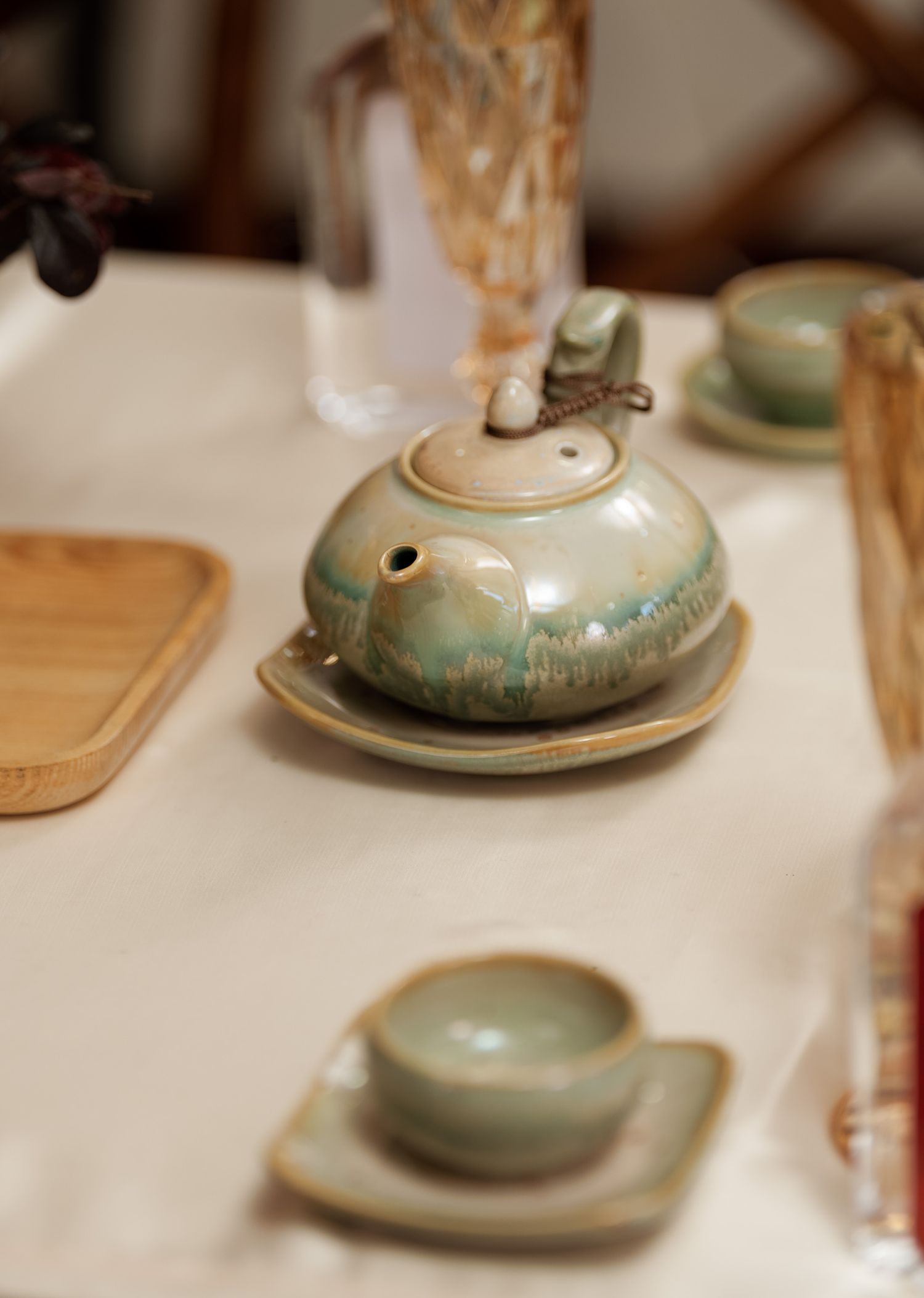 Ceramic teapot and cups in soft celadon green on white tablecloth.