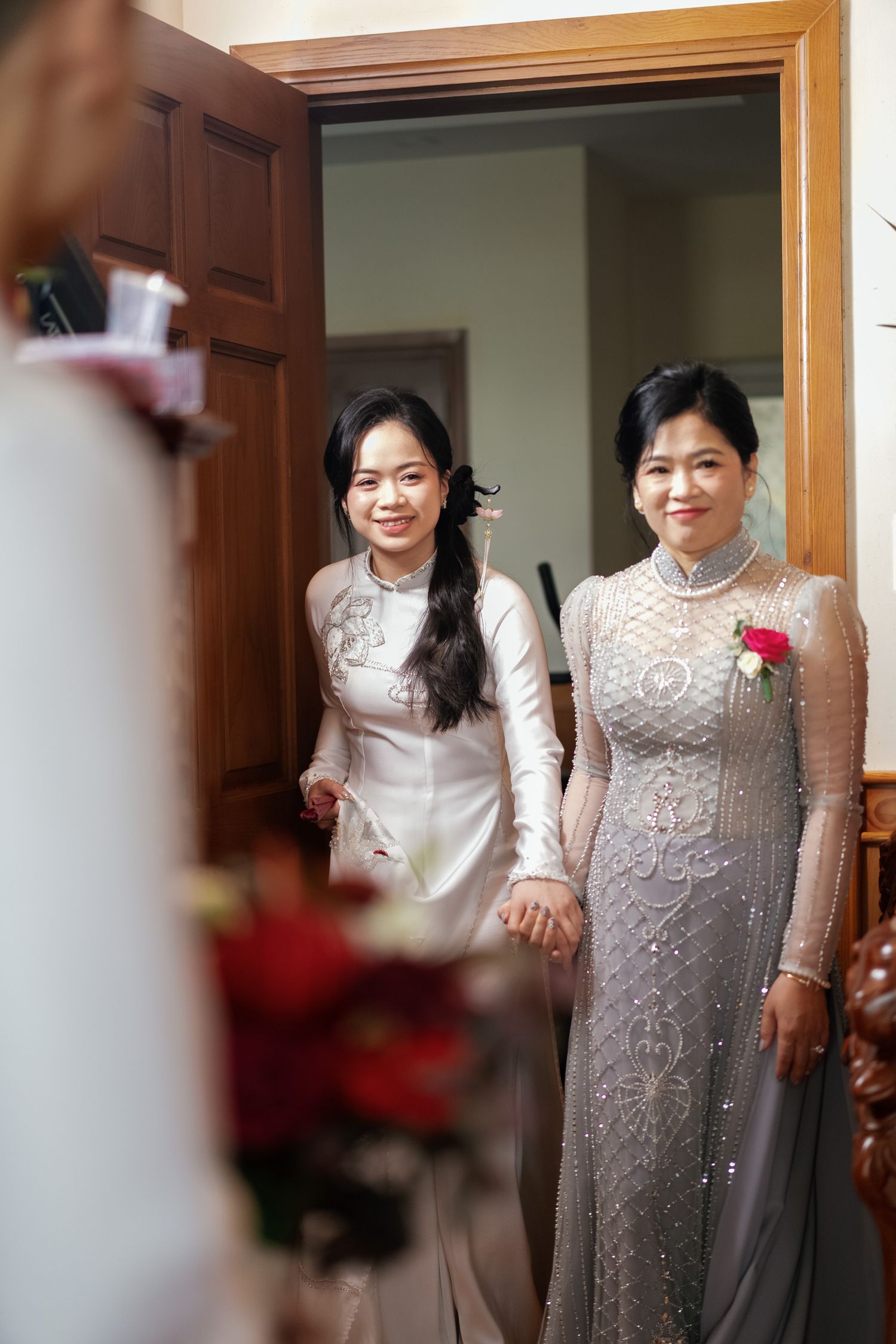 Two people in traditional white and gray ao dai dresses stand in doorway.