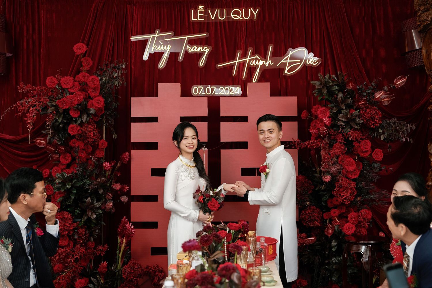 Traditional Vietnamese wedding ceremony with red decor and double happiness symbol backdrop.