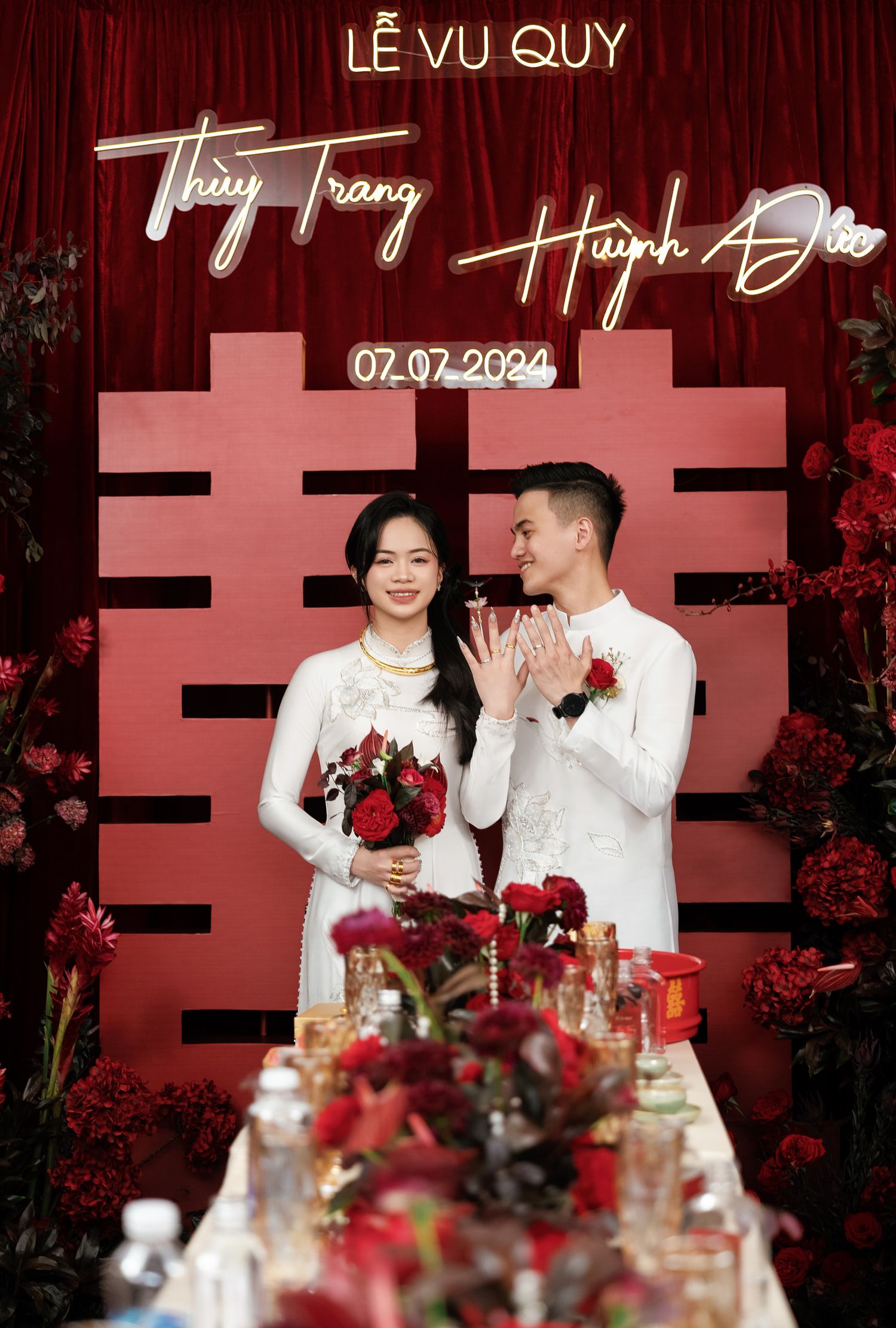 Wedding photo with couple in white against red backdrop with Chinese double happiness symbol.