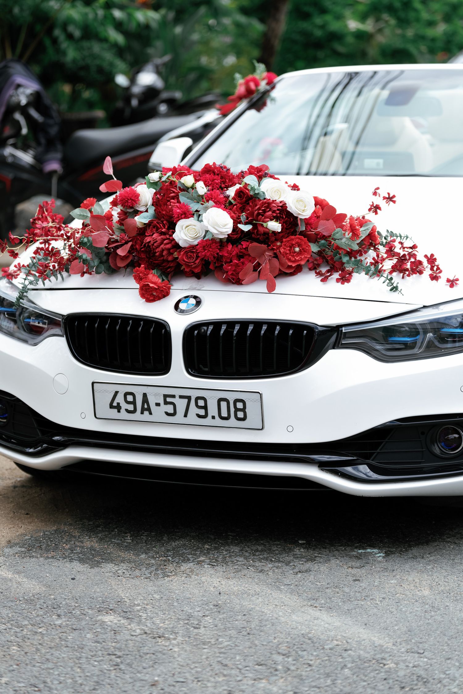 White BMW decorated with red and white floral arrangements on the hood for a wedding ceremony.