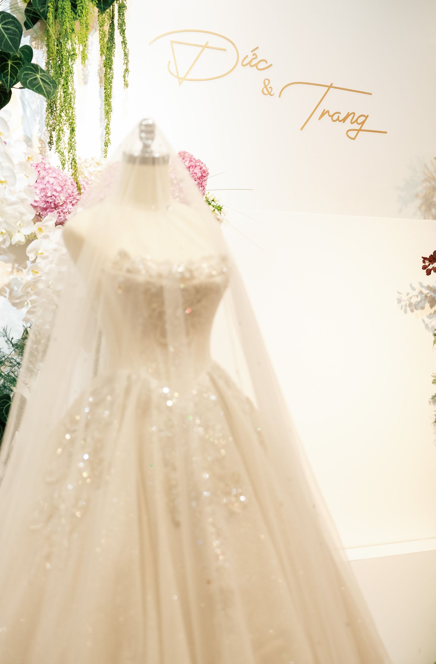Elegant white wedding dress on display with hanging greenery and floral accents.