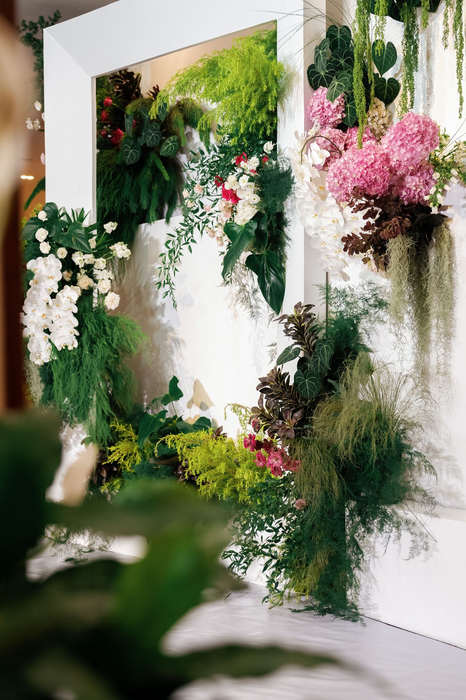 Luxurious floral wall installation featuring white orchids, pink blooms and cascading greenery.
