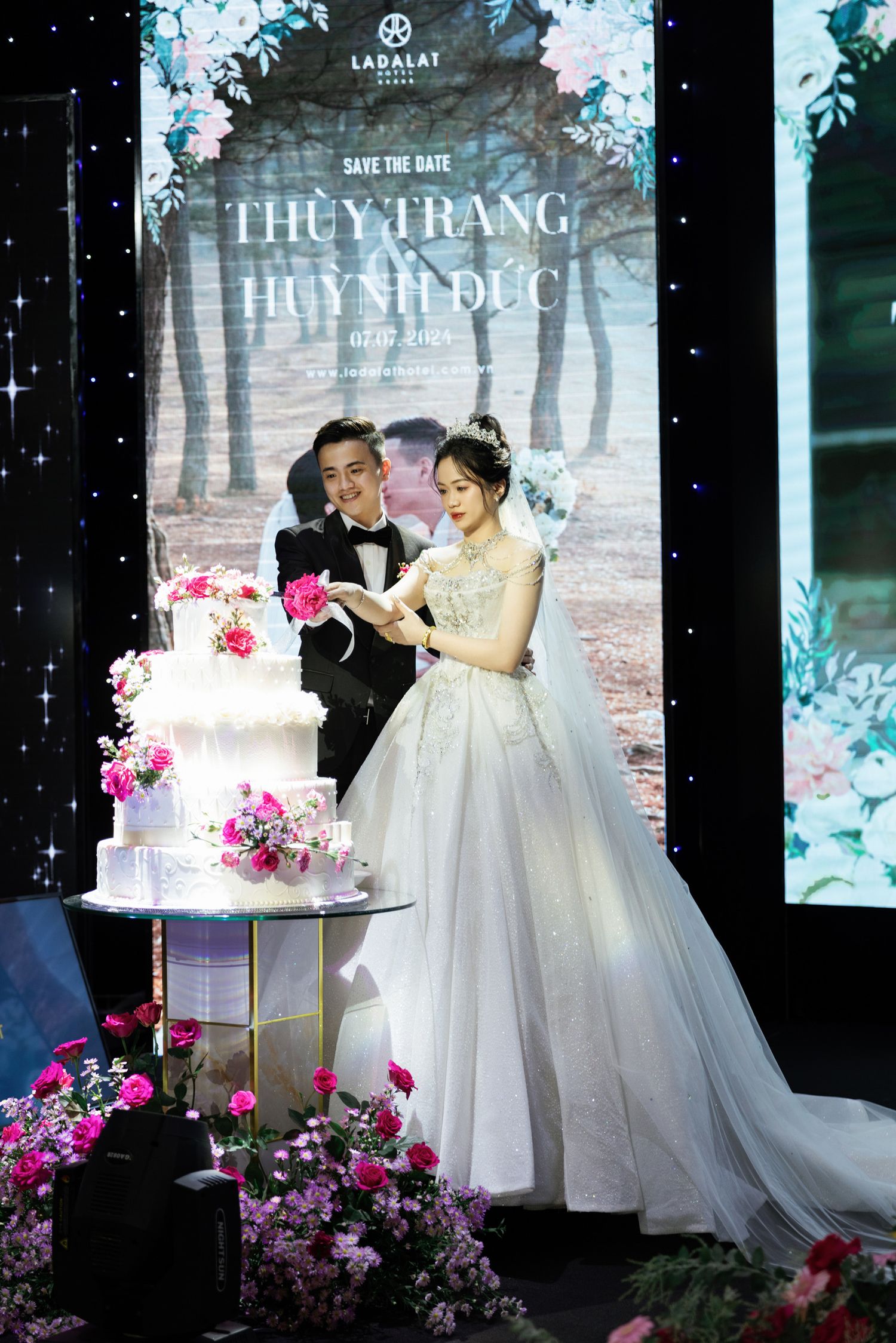 Wedding celebration with elegant tiered cake decorated with pink flowers.