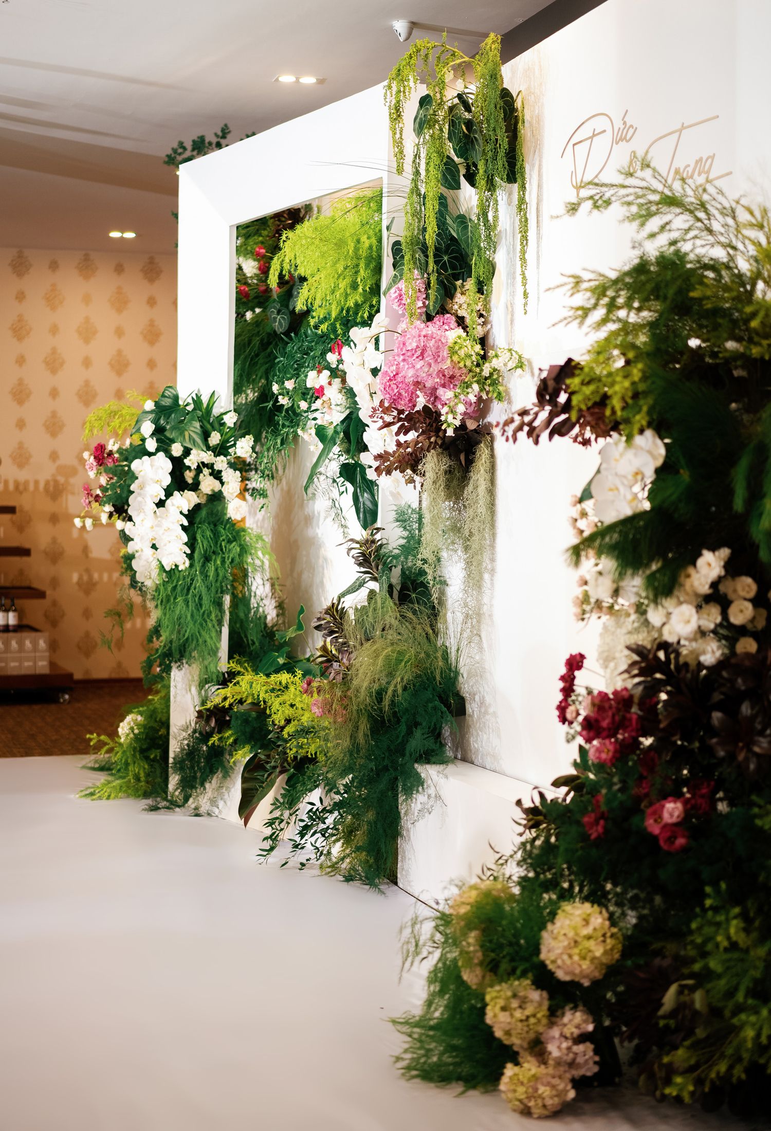 Elegant floral wall display with cascading greenery and mixed pink and white flowers against a white backdrop.