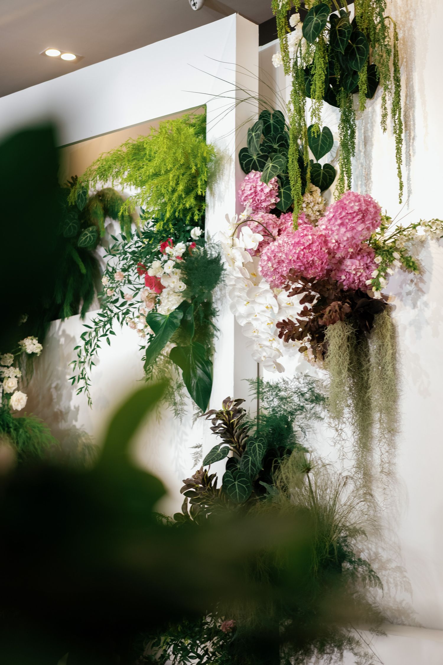 Lush botanical installation featuring pink hydrangeas and trailing greenery on a white wall.