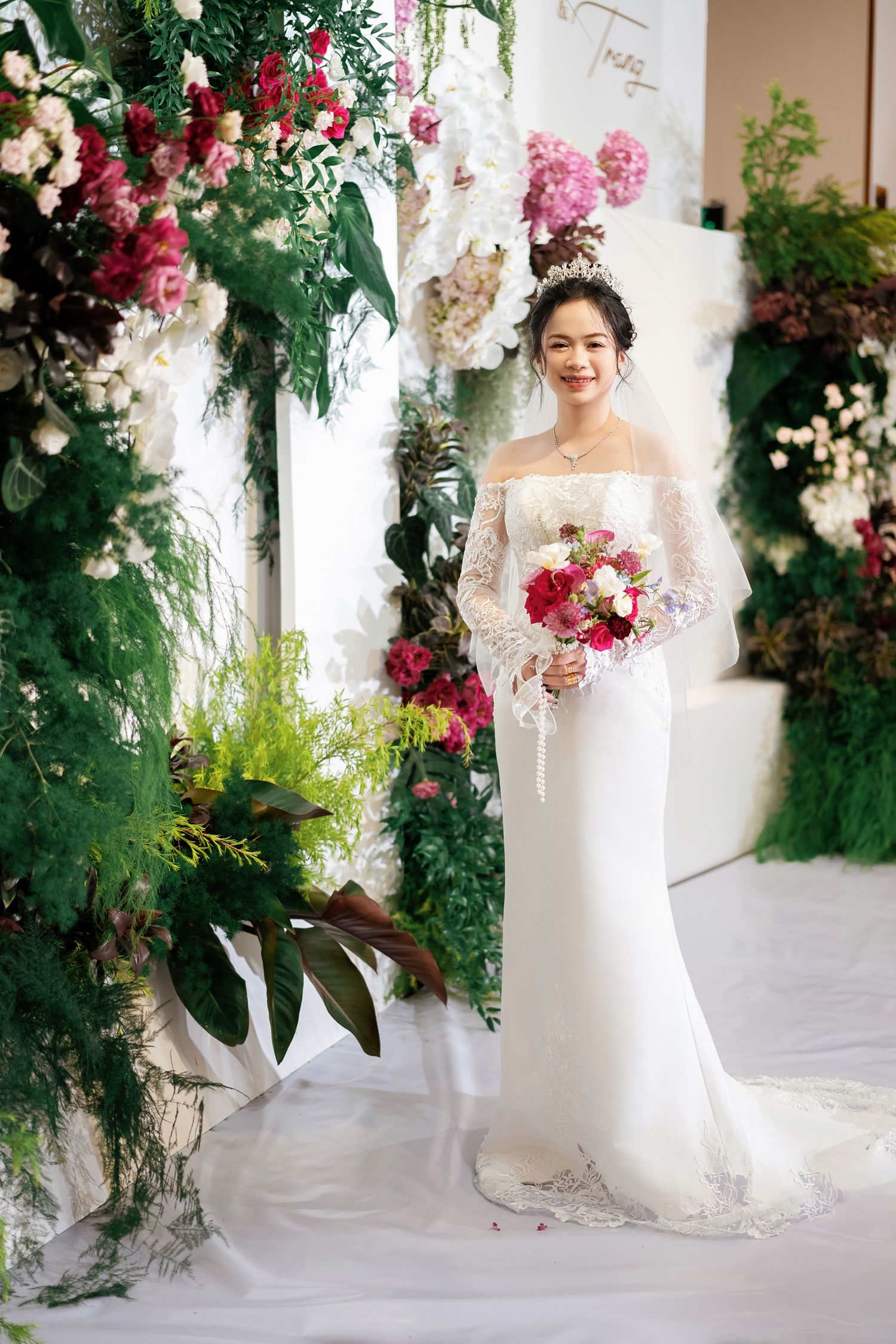 Elegant wedding setup with lush floral arch featuring pink and white blooms against a white backdrop.