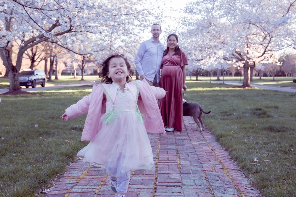 Young child in pink dress dances joyfully under blooming cherry blossom trees.