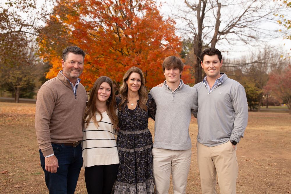 Family of five poses outdoors against vibrant fall foliage in coordinated casual attire.