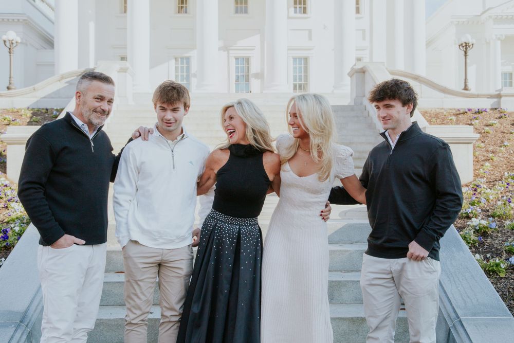 Group poses on white stone steps in coordinated formal attire at historic building.