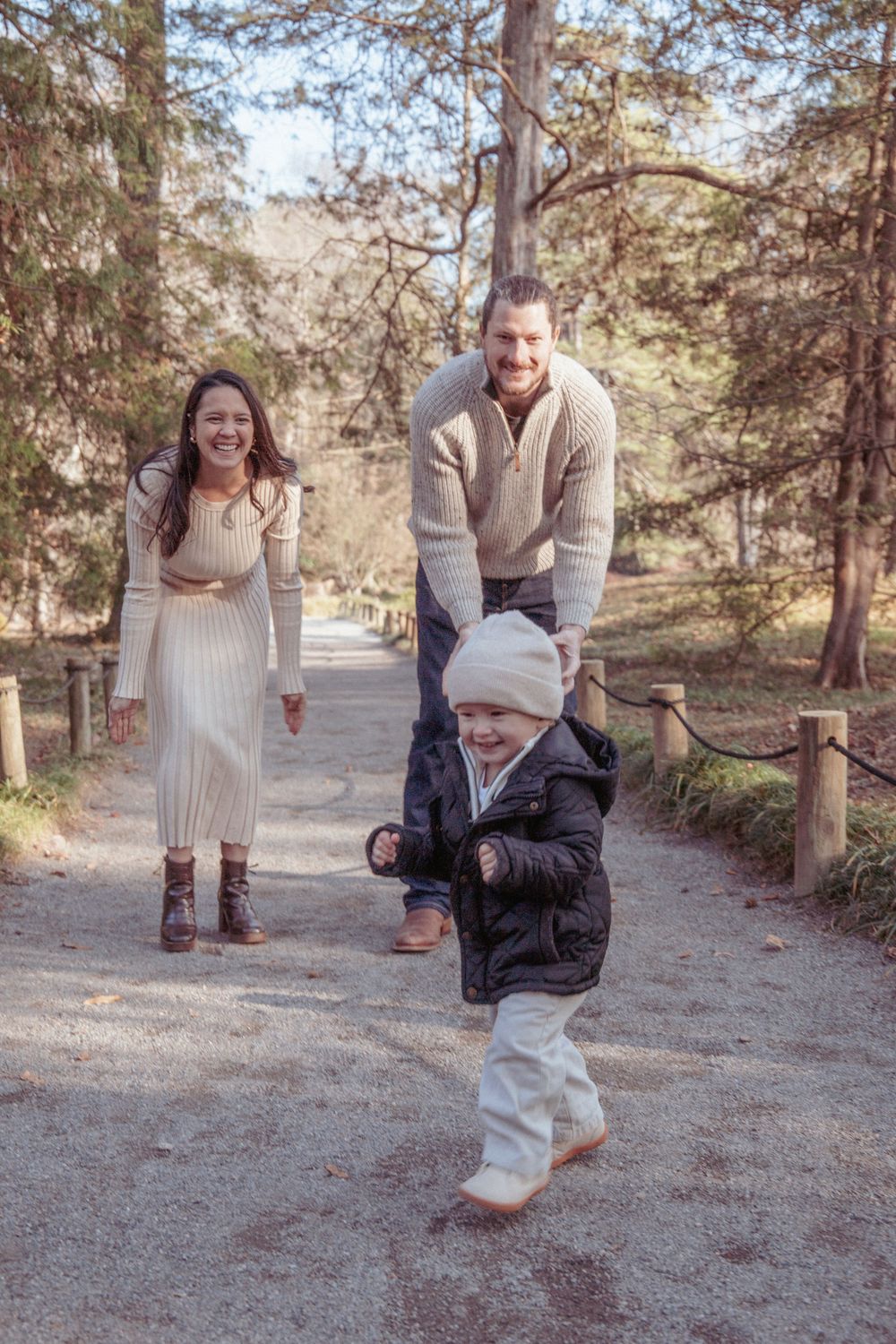 Family moment captured on nature trail as toddler takes steps with support.