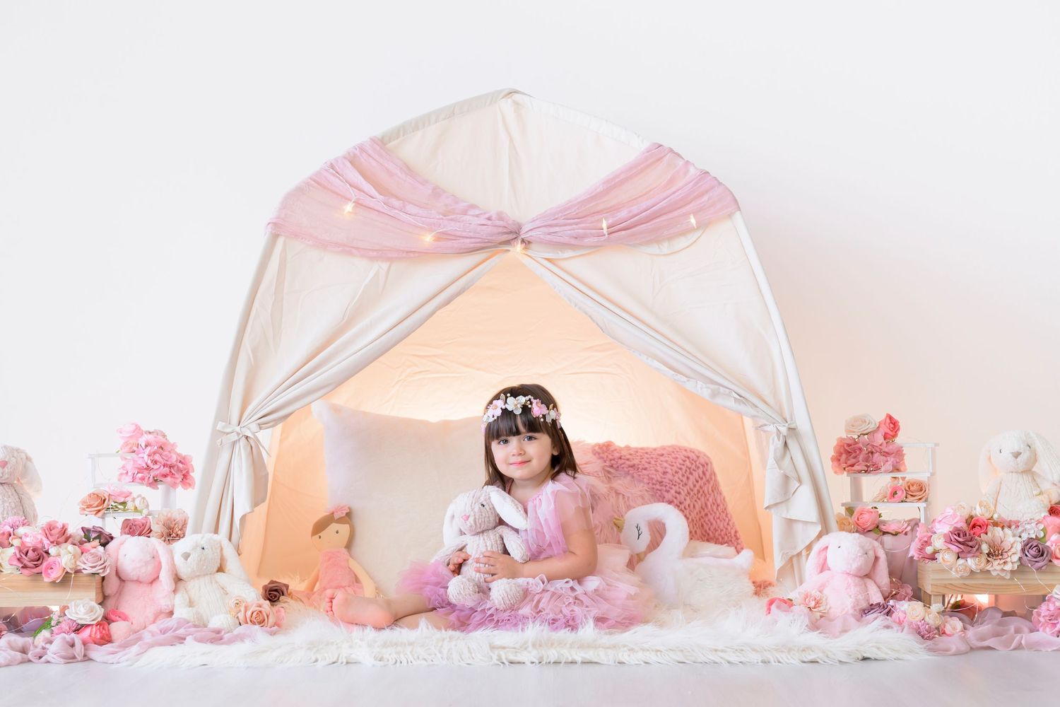 Dreamy pink teepee tent decorated with flowers and fairy lights creating a magical children's play space.