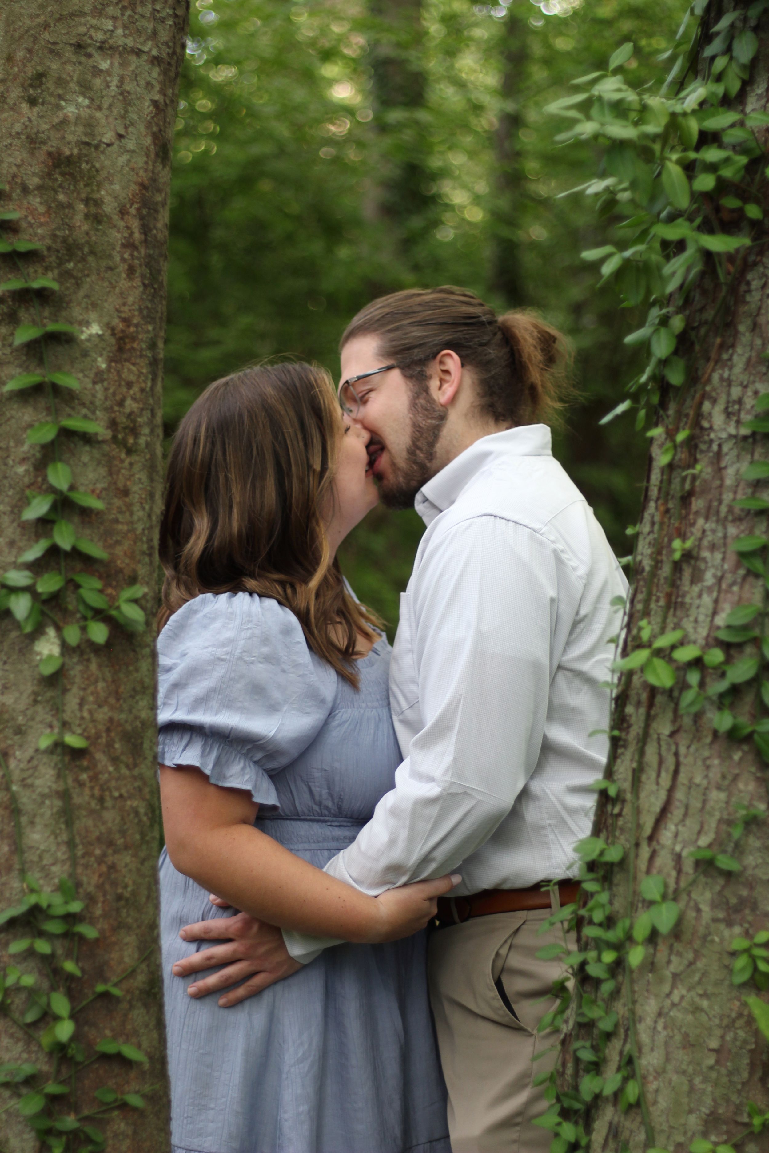 A couple dreamily kissing in the woods.