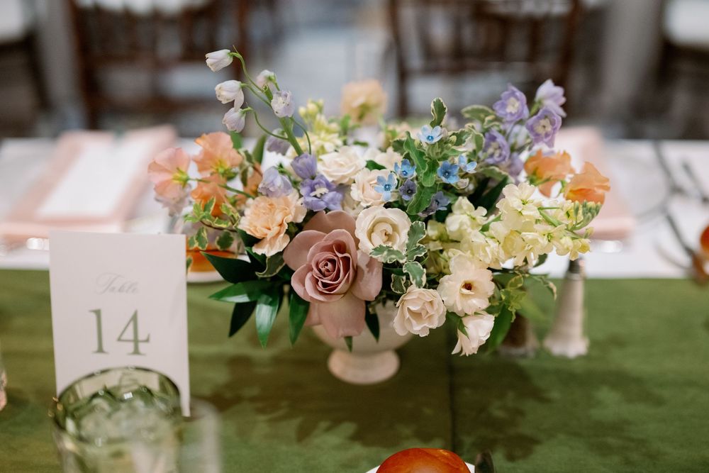 Elegant wedding centerpiece with pastel roses, lavender, and mixed blooms in a white vase beside table number 14.