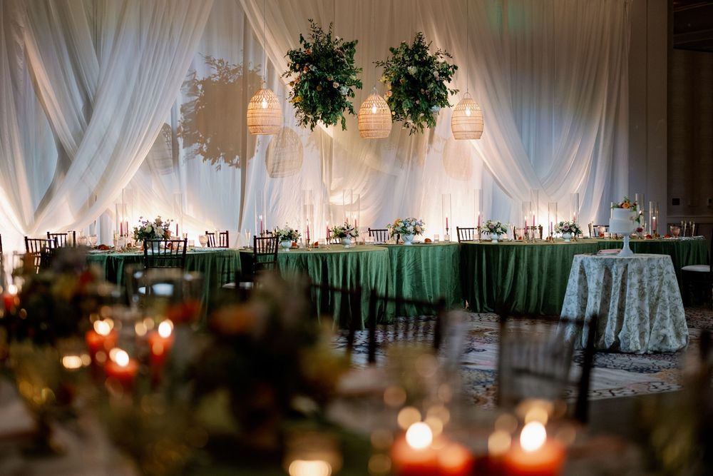 Elegant wedding reception with green draped tables, floral ceiling installations, and warm candlelight ambiance.