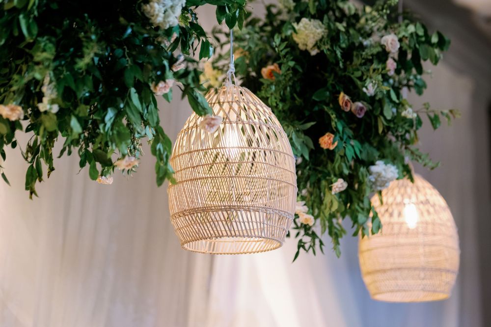 Woven rattan pendant lights hanging beneath lush greenery and white floral arrangements at an elegant wedding reception.