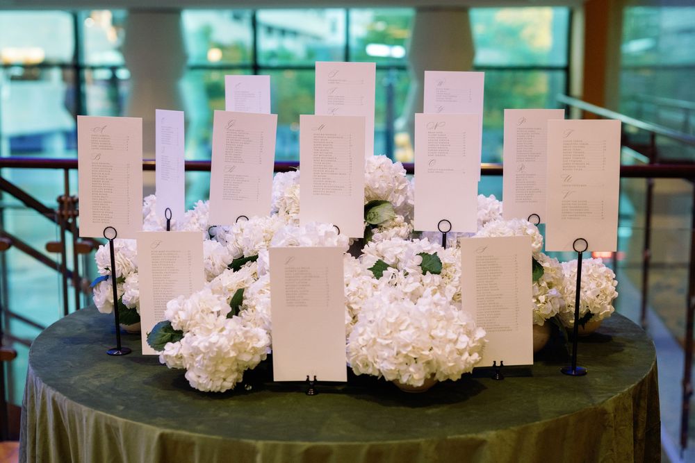 Elegant wedding seating chart display with white cards arranged among lush white hydrangea floral arrangements on a draped table.