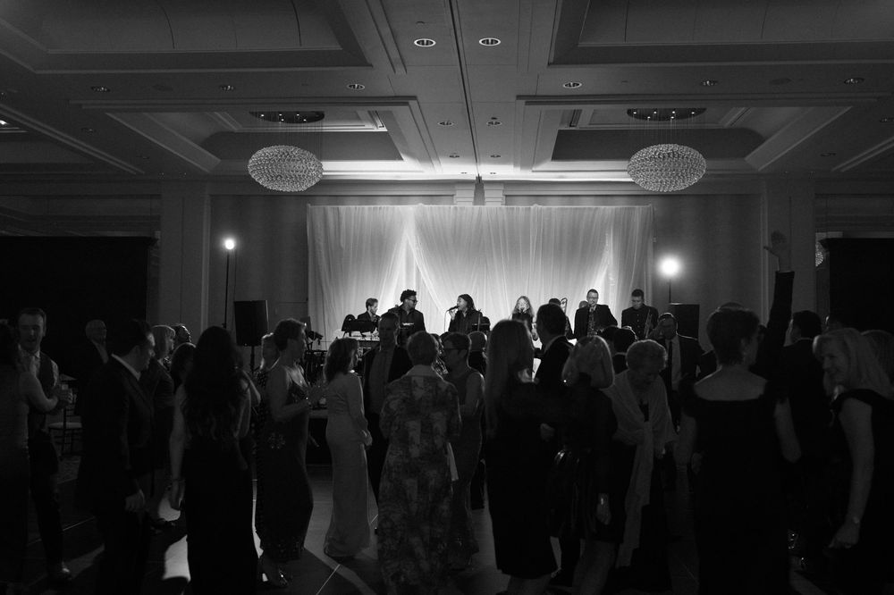 Black and white photo of wedding reception guests dancing on a ballroom floor with a live band performing on stage.
