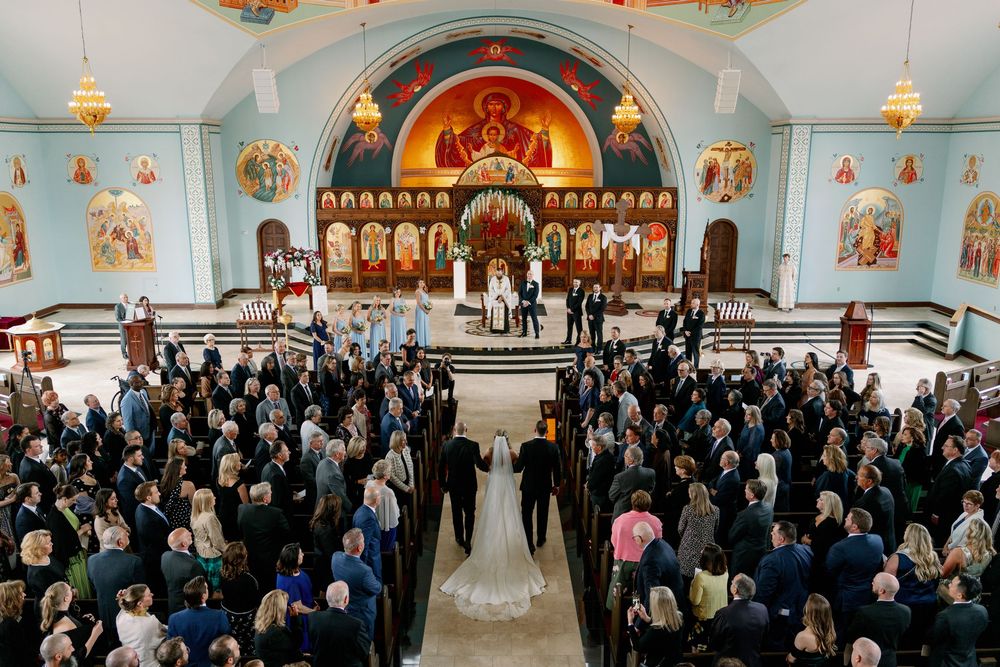 Wedding ceremony inside ornate Orthodox church with full congregation and bridal party at altar.