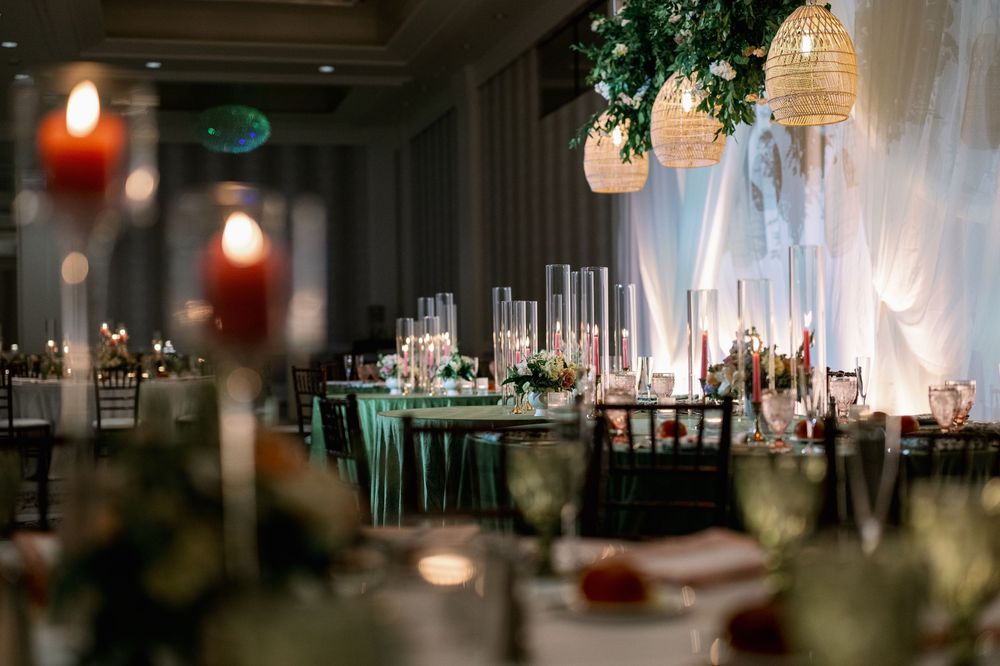 Romantic wedding banquet setup featuring candlelit tables, green linens, floral arrangements, and woven hanging lights.