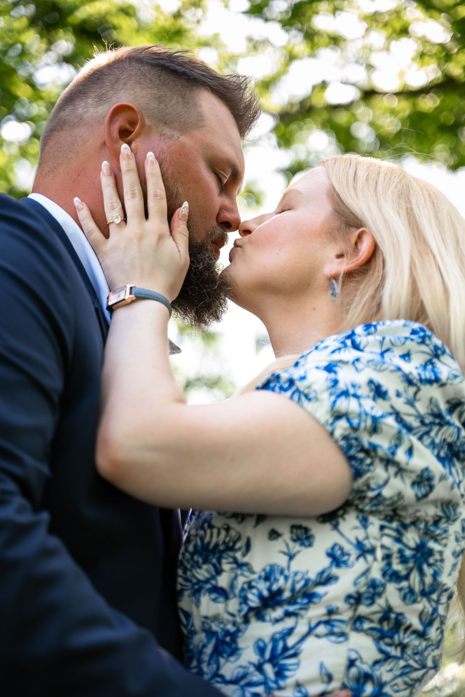 Close-up of couple about to kiss with engagement ring in focus and Powell Gardens in the background