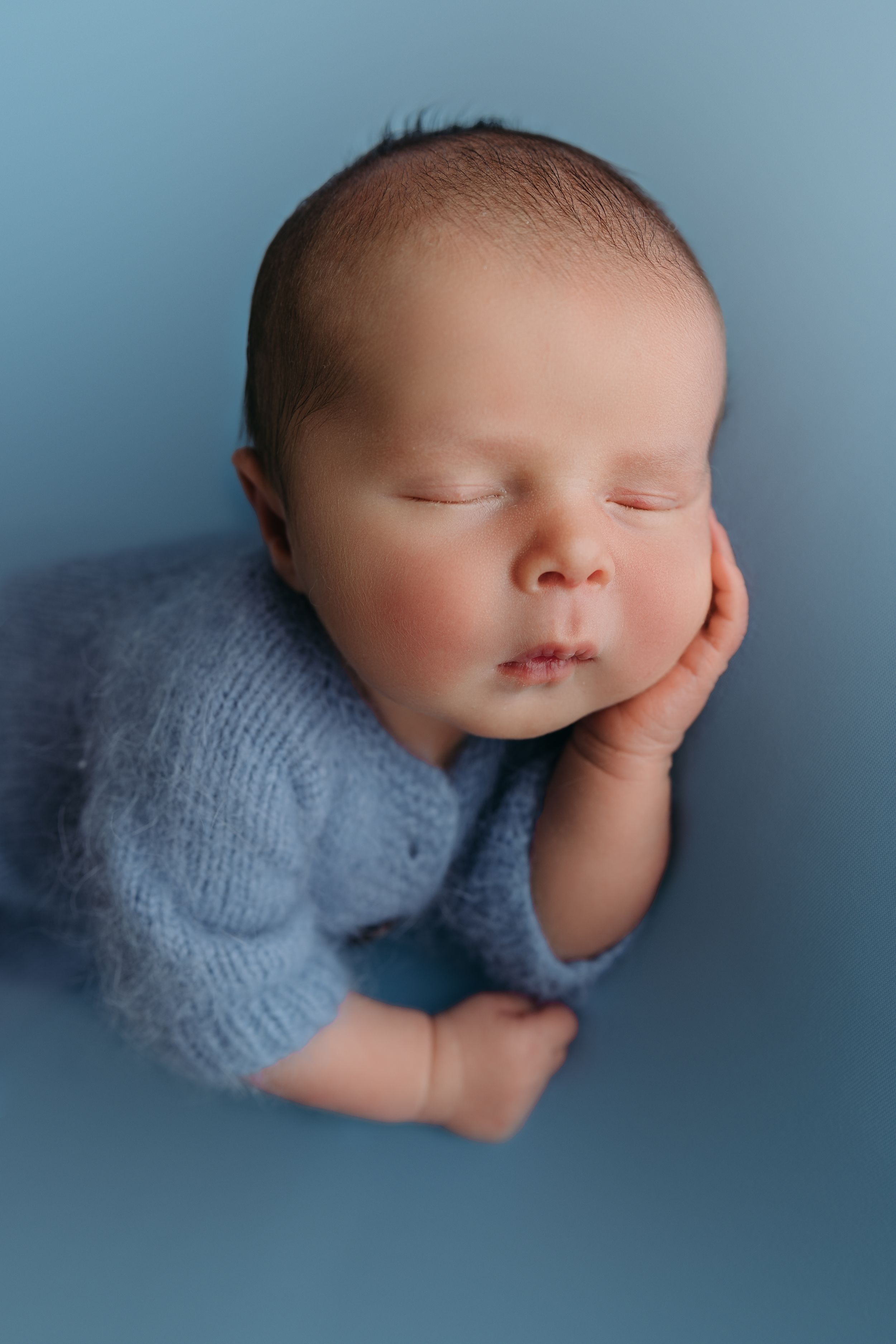 Newborn baby sleeping peacefully in a soft gray sweater against a blue background, captured from different angles.