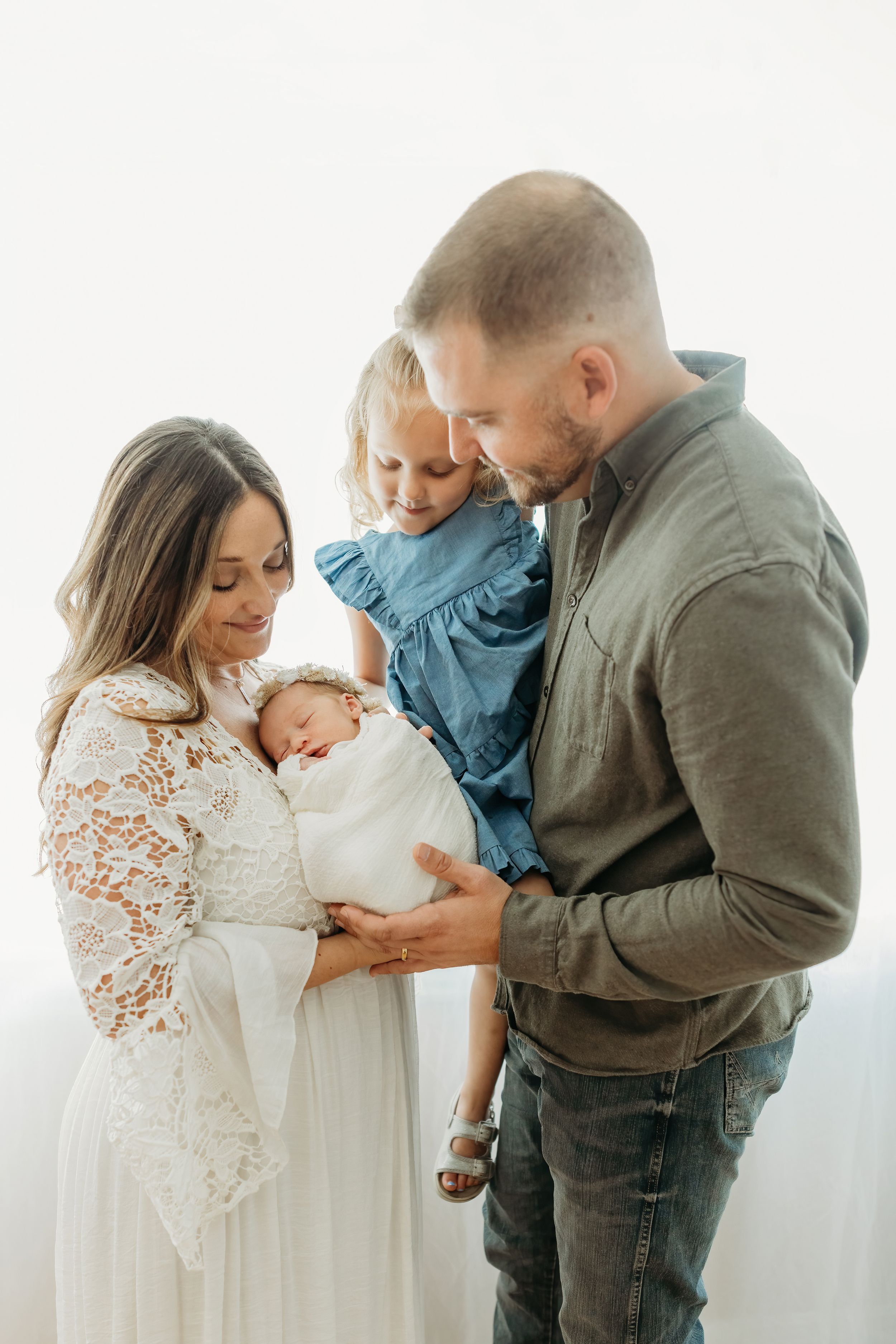 A family shares a tender moment together as they gather around their newborn baby wrapped in white.