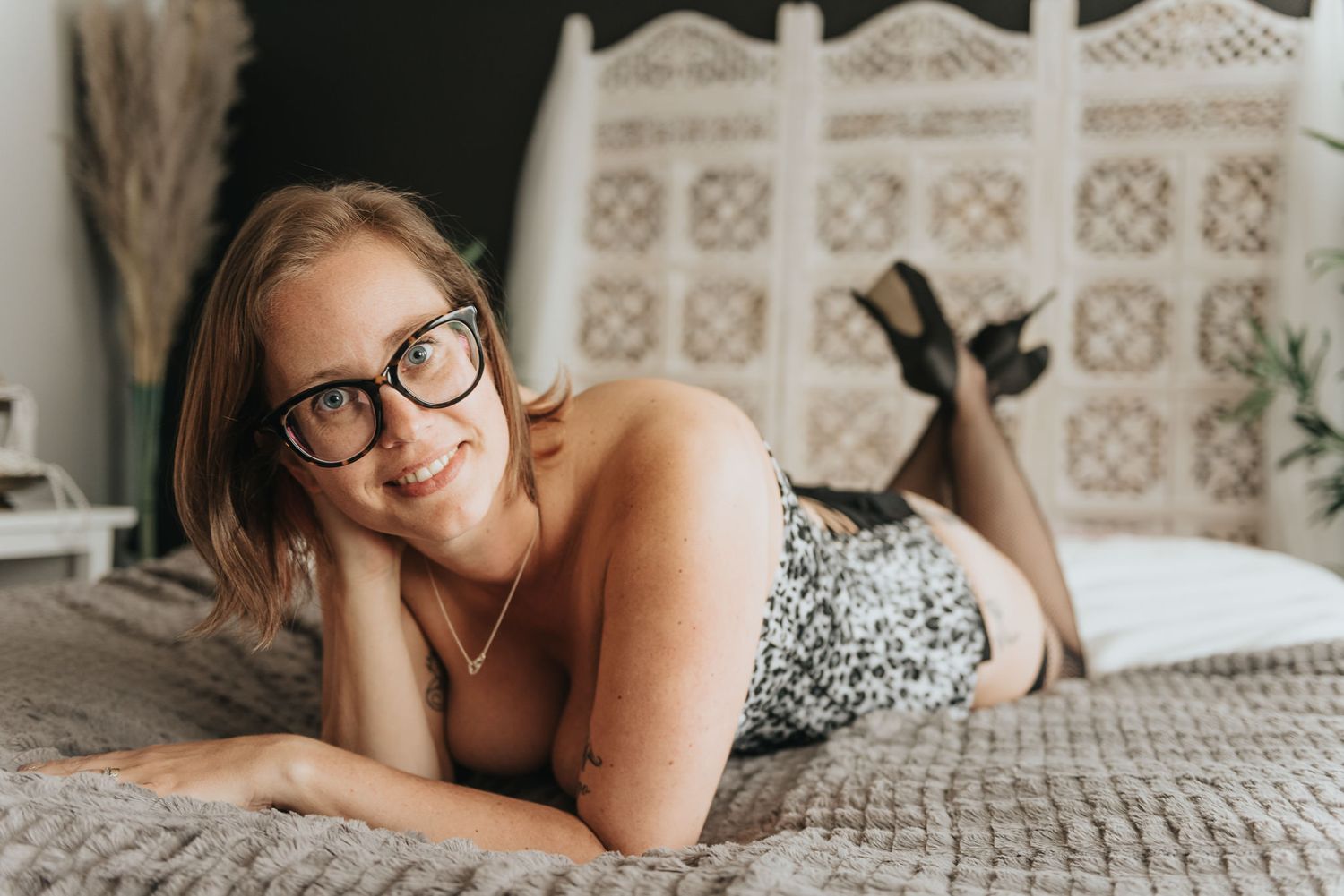 Leende tjej liggandes i boudoirstudio sängen med en snygg body och högklackade skor.