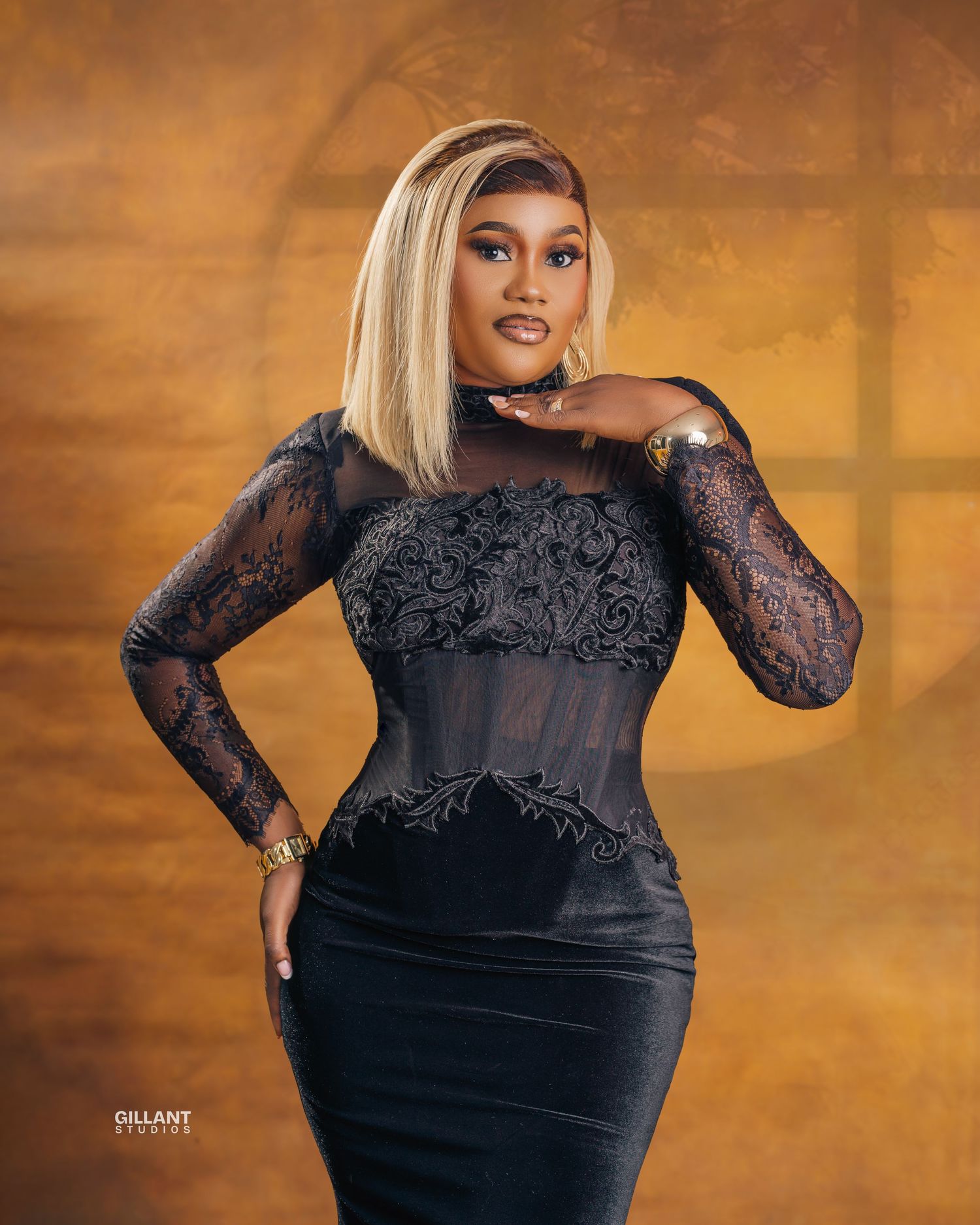 Fashion portrait featuring elegant black lace dress against warm golden background.