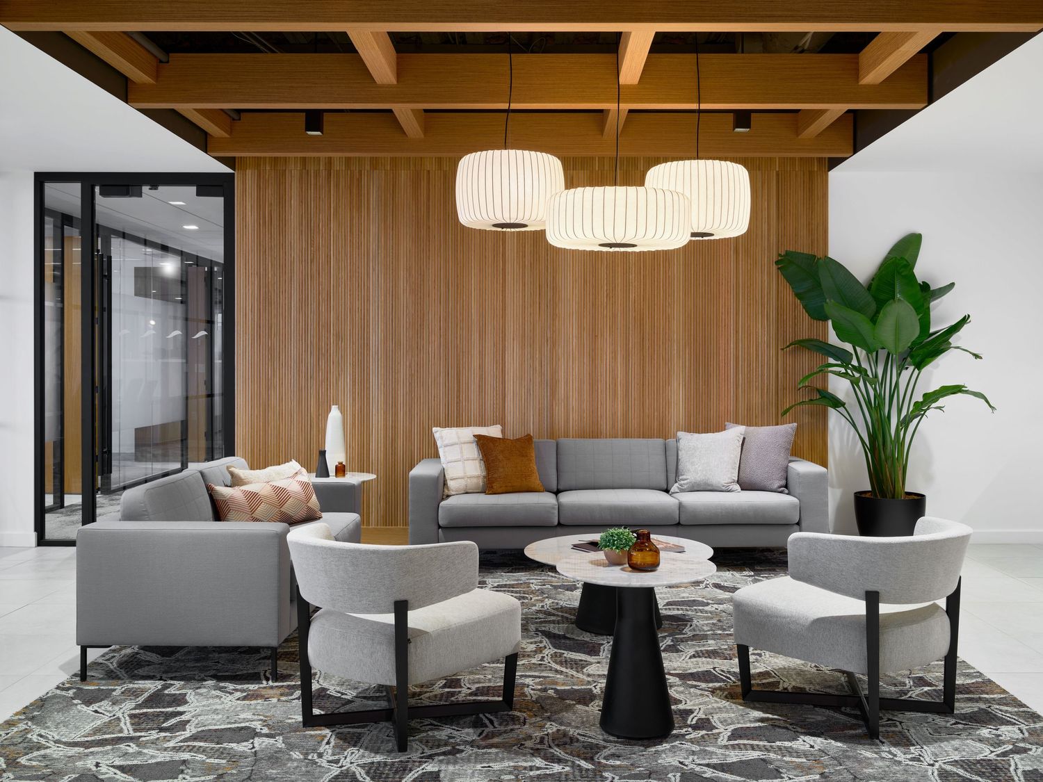 A modern open-concept office features wood paneling, gray furniture, and pendant lighting with lush plants and natural light.