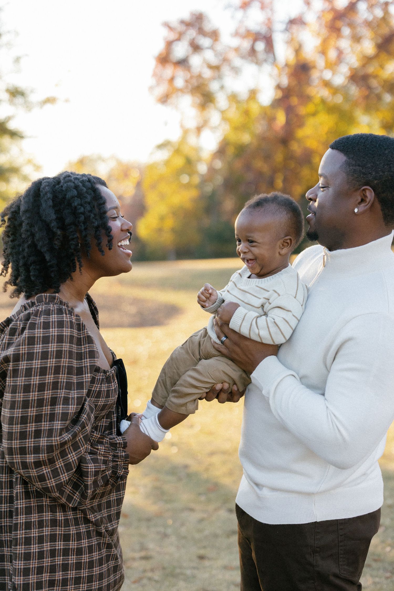 A family lies together on grass during golden hour while sharing tender playful moments in a park.