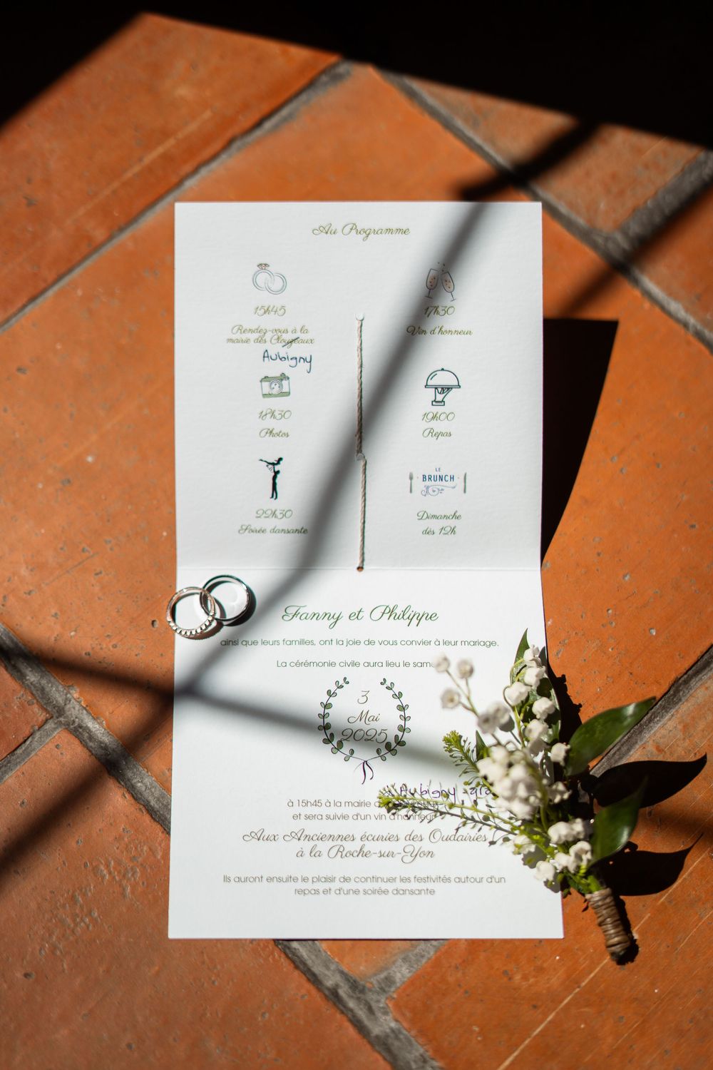 Wedding invitation with wedding rings and delicate white flowers on terracotta tiles with dramatic lighting.