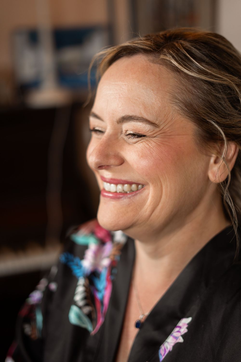 A woman in a black floral robe laughs joyfully with closed eyes in a candid portrait.