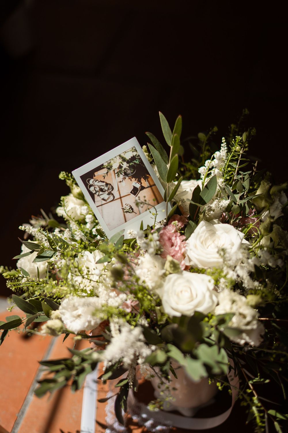 Elegant white and pink floral arrangement with roses and greenery sits beside a vintage polaroid photo in soft lighting.