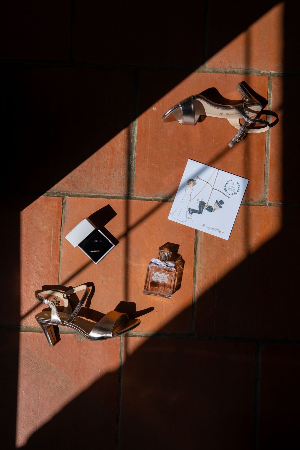 Wedding accessories and perfume bottle arranged in diagonal slices of sunlight on a textured terracotta wall.