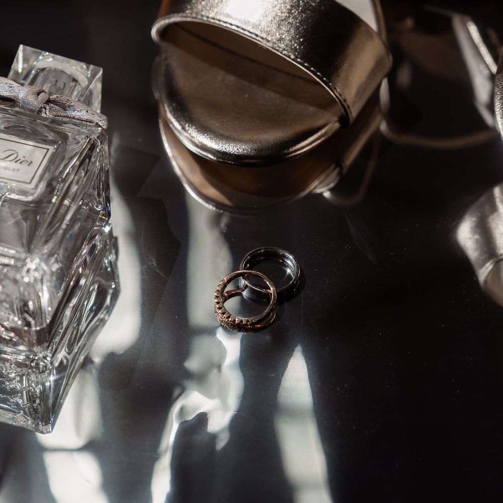 Wedding rings artistically photographed with perfume bottle and metallic shoes.