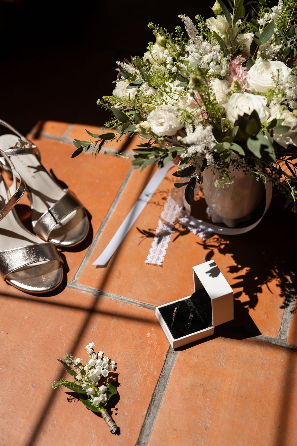 Wedding place settings on a terracotta table with floral centerpieces and shadows cast across the surface.
