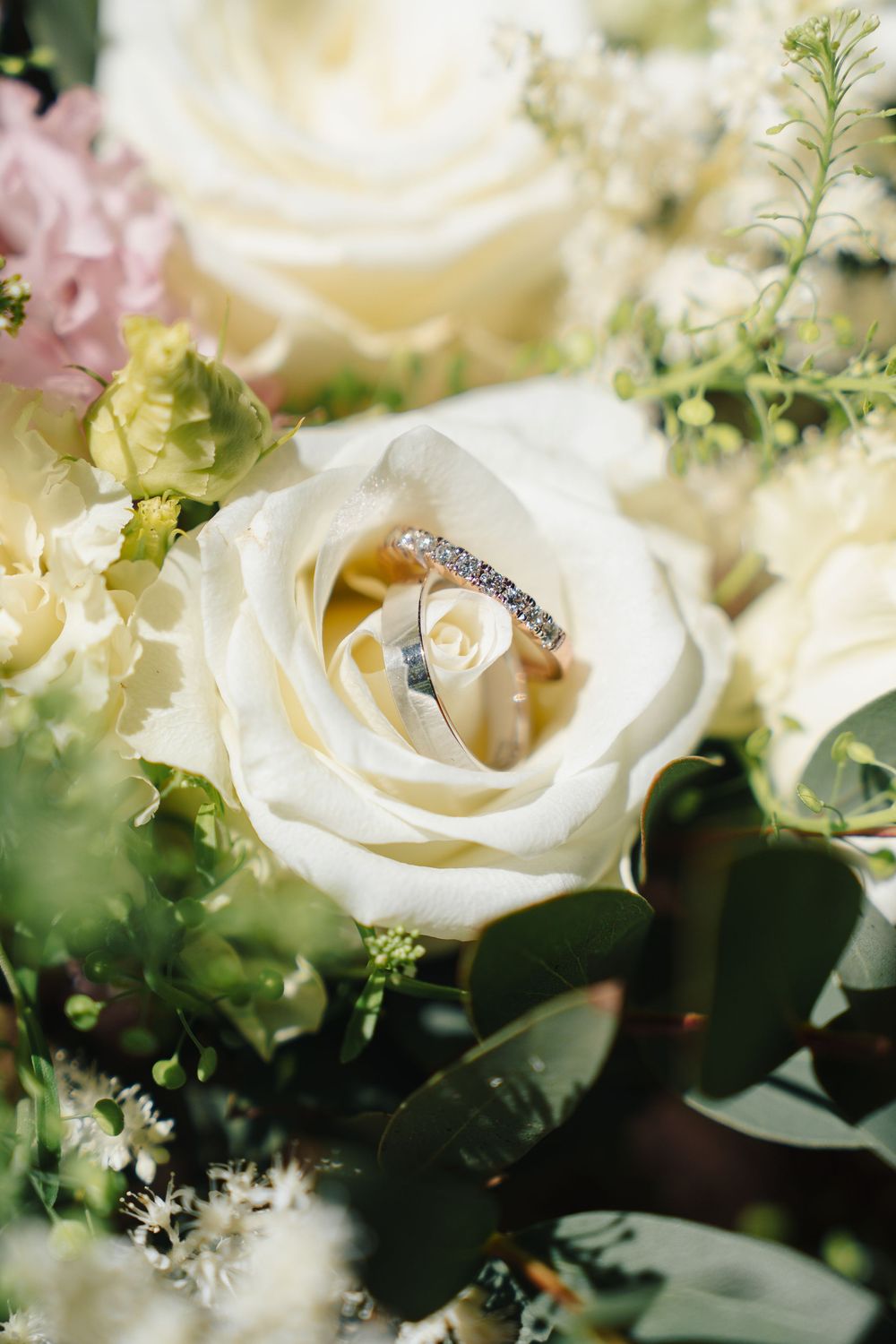 Diamond wedding ring nestled within delicate white roses and greenery in an elegant floral arrangement.