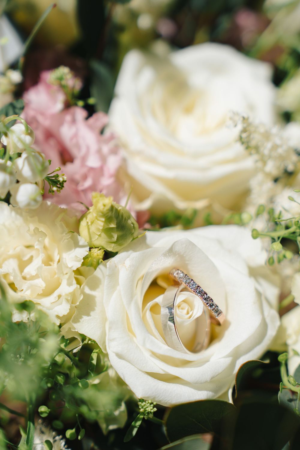 Wedding rings nestled in white and pink roses with delicate greenery.