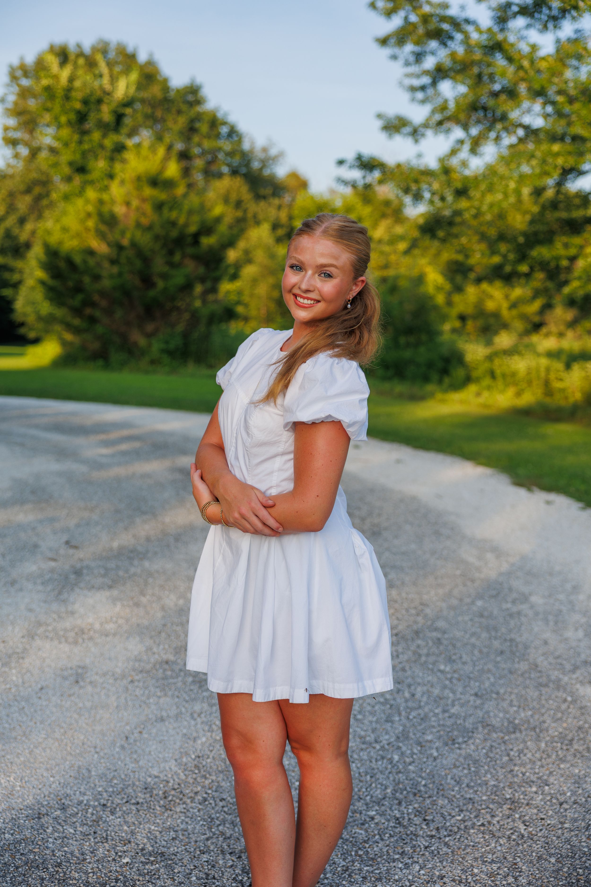Summer photoshoot on a gravel path surrounded by lush green trees.