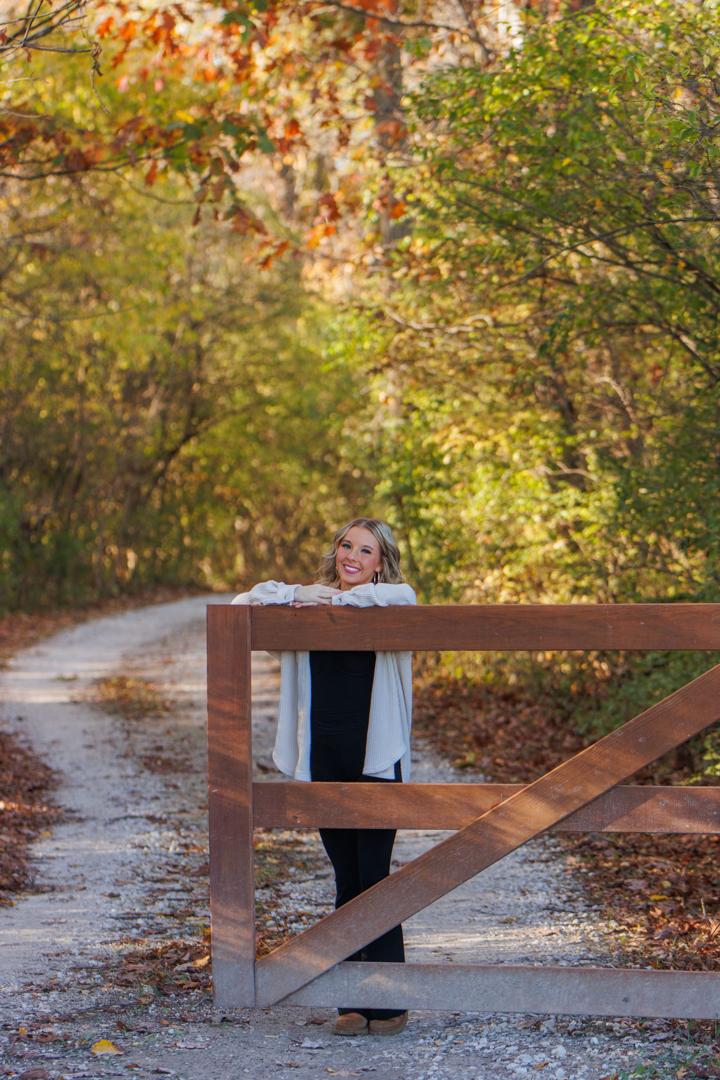Wooden fence along an autumn path with fallen leaves and natural foliage. A senior girl posing by a fence.