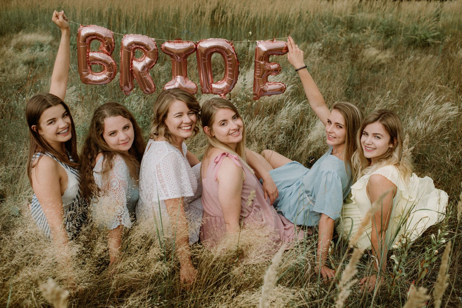 Friends pose joyfully together in a summer field during golden hour.