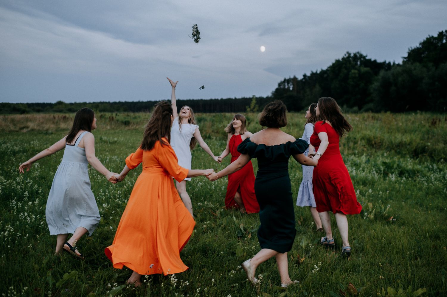 People in colorful dresses dance and twirl together in a flowering summer meadow.