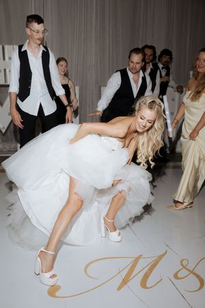Joyful blonde bride in white ball gown dancing energetically on monogrammed dance floor.