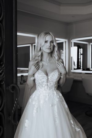 Elegant bride in lace ballgown wedding dress posing in bridal suite mirror.