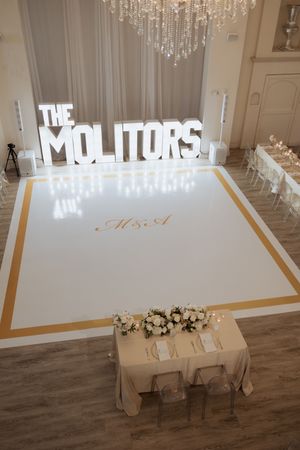Elegant wedding reception venue with illuminated THE MOLITORS marquee letters above a white and gold dance floor.