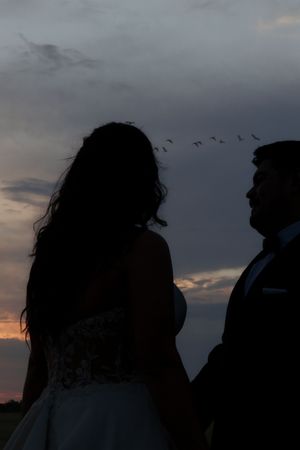 Silhouettes of people against a dramatic sunset sky with dark clouds and warm orange light peeking through.