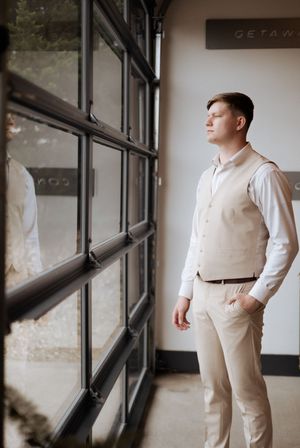 A person in a beige vest and white shirt gazes thoughtfully through a large modern window.