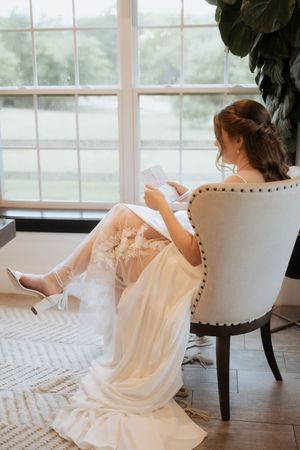 Young child in white ruffled dress sitting in elegant studded chair near windows creating dreamy sequence.
