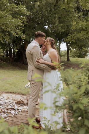 A wedding couple shares romantic kisses in a natural outdoor setting with trees and rocks in the background.